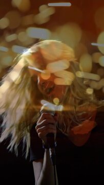 Vertical video: Lead singer singing into mic on music stage tossing hair, bokeh reacting for crowd