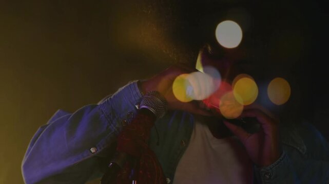 Vertical video: Male musician lifting harmonica to mouth, playing mic for music, bokeh around hands