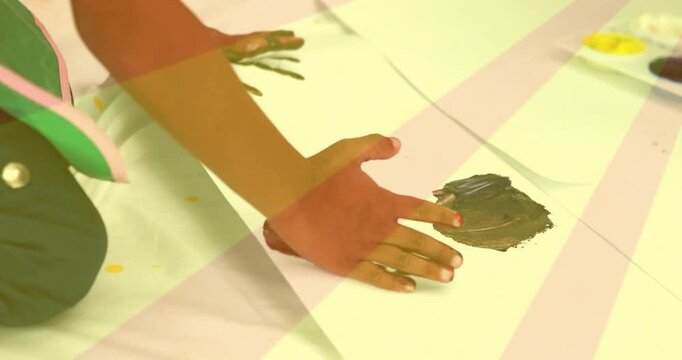 Child pressing painted palms into brown paint, making two handprints on white paper for craft