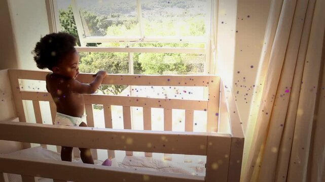 Baby standing in crib reaching toward open sash after sunlight drawing attention, steadying on rail