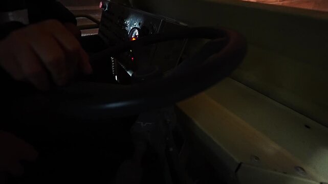 A first-person view from inside a vehicle shows a hand on the steering wheel as a dusty windshield frames a construction site outside, conveying focus, travel, and rugged work.