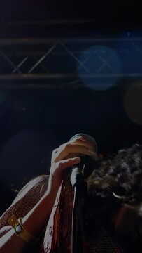 Vertical video: Female singer opening mouth, singing into mic on stage, hair whipping for audience