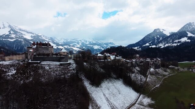 Aerial: Gruyeres Castle with snow and mountains during the day in Canton of Fribourg, Switzerland, orbit drone shot