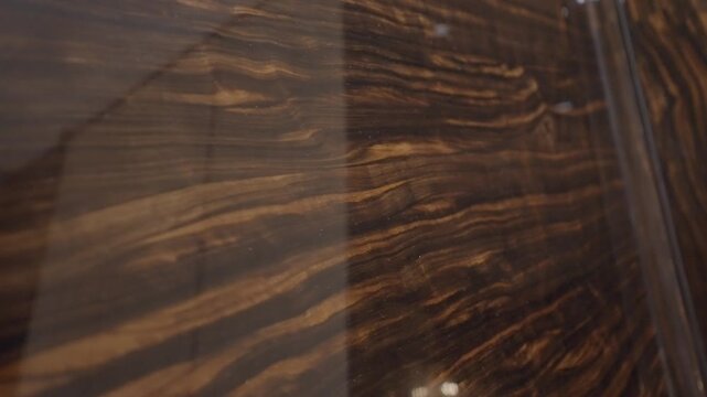 Close view of glossy brown marble wall with golden veins, camera sliding along polished surface indoors.