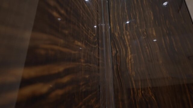 Low angle view of glossy brown marble panels with golden veins and ceiling light reflections.