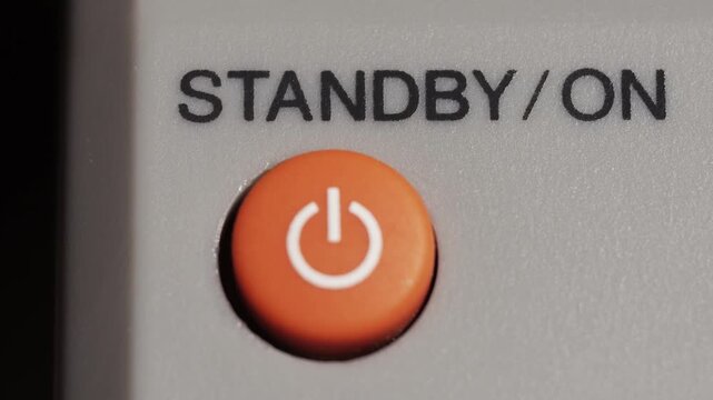 Macro close up of orange power button pressed on grey device with black standby text