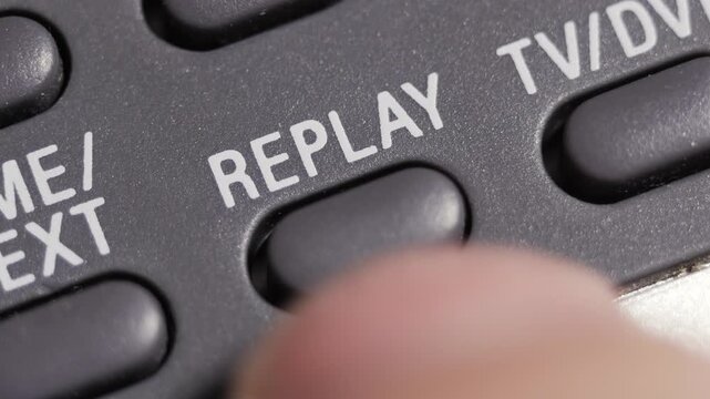 Macro close up of replay button pressed on dark grey remote with white lettering