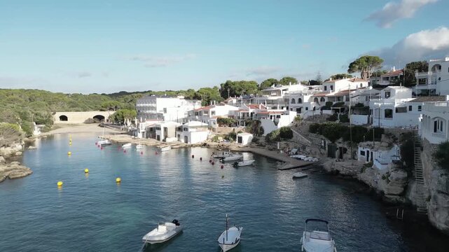 Drone pullback from Alcaufar cove revealing the fishing village, small boats floating in turquoise water, and the calm Mediterranean atmosphere in early morning light.