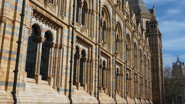 Detailed side view of the Natural History Museum in London showcasing its iconic Romanesque architecture, striped stone facade, and repeating arched windows. The intricate design highlights