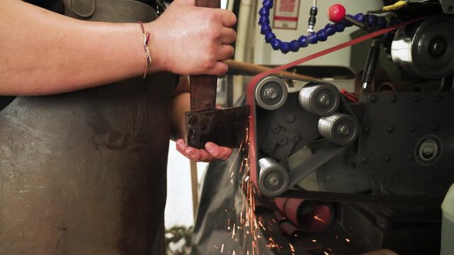 A hatchet is being sharpened on a grinding machine in Malaysia, with sparks flying, highlighting tool maintenance, precision work, and industrial craftsmanship. Slow motion close-up . UHD.