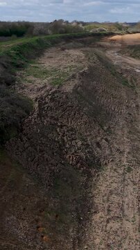Panshanger quarry vertical drone pullback reveals rugged dirt tracks, gravel embankments, sand and green scrub under bright spring light and scattered clouds in rural Hertfordshire, England.