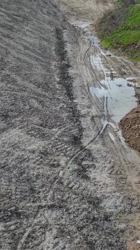 Vertical drone flight through Panshanger quarry valley, Hertfordshire, England. Low forward aerial pass over muddy tracks, gravel slopes, puddles and exposed earth in an active excavation landscape.