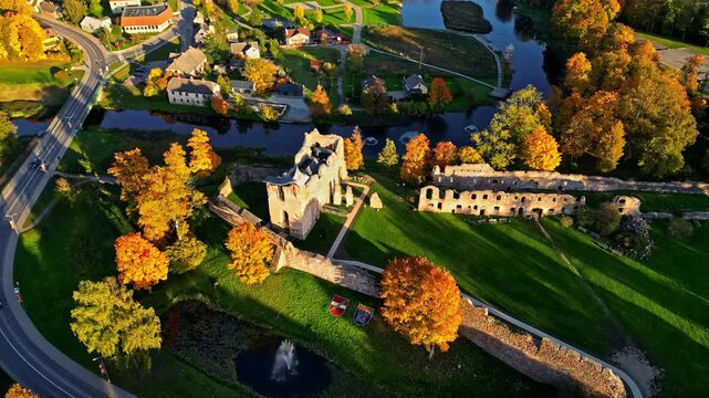Dobele Castle ruins surrounded by autumn trees and river with nearby houses, Dobele, Latvia