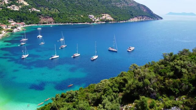 Sailboats in the calm turquoise Rouda Bay surrounded by lush green mountains. Mediterranean summer bliss, aerial of Mikros Gialos beach, Lefkada, Greece