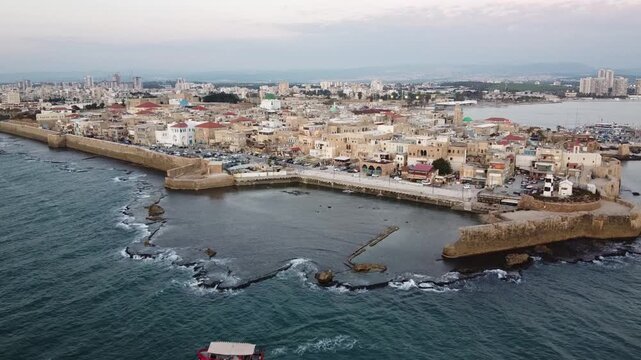 Aerial view of the Old City of Acre Akko, Israel, red boat cruising past the ancient sea port during twilight