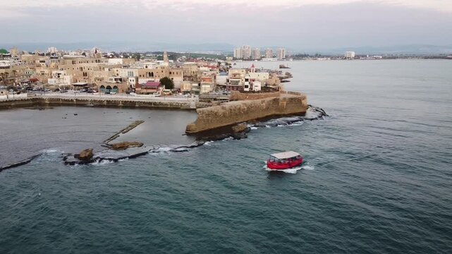 Twilight aerial of small red boat crossing the ancient sea walls and heritage architecture of Akko, Old City of Acre in Israel