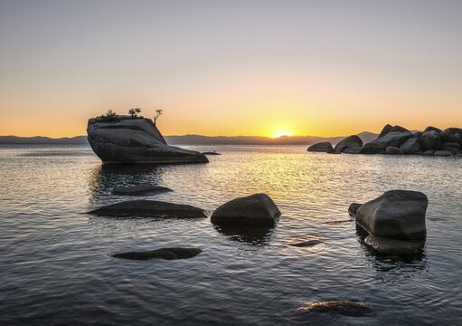 View of Bonsai Rock, small tree on a rock in the water at sunset, round stones in the water, Lake Tahoe, California, USA