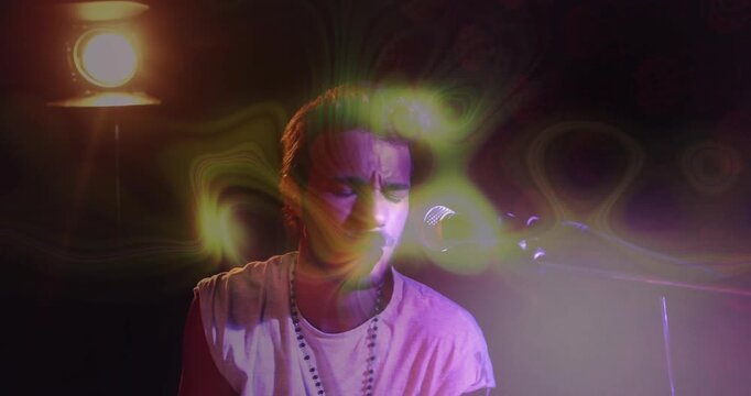 Male singer focusing then raising arm, leaning into mic and singing with lamp and lights swirling
