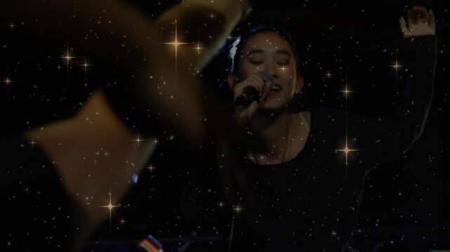Female singer responding to fans reaching, leaning singing into concert mic with sparkle overlay