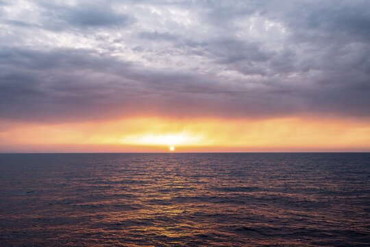 View across the open sea to the setting sun, dramatic cloudy sky at sunset, Rhodes, Dodecanese, Greece