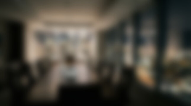 Blurred interior scene with people, modern room with large windows and city view, abstract background with bokeh effect, indoor setting with undefined elements.