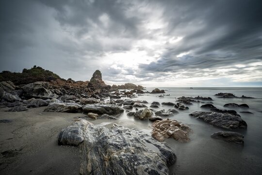 Rocky coast, rocks on the beach, dark rain clouds, long time exposure, West Coast, South Island, New Zealand