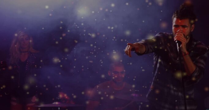 Lead vocalist stepping inward, performing to engage crowd in music, drawing sparkles over drum kit