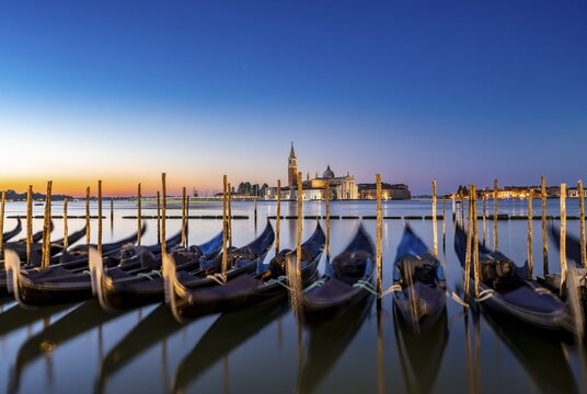 Venetian gondolas, boat dock at St Mark's Square, church of San Giorgio Maggiore in the background, long exposure at sunrise, Venice, Veneto, Italy