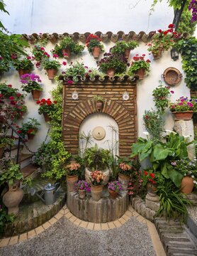 Fountain in the courtyard decorated with flowers, geraniums in flower pots on the house wall, Fiesta de los Patios, C&oacute;rdoba, Andalusia, Spain