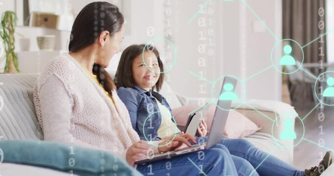 Vertical video: Mom or girl on sofa typing laptop tapping tablet binary icons moving over tech shari