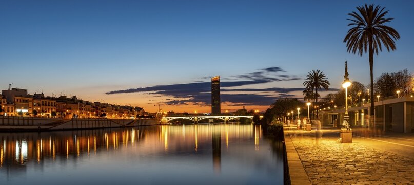 View over the river Rio Guadalquivir with illuminated bridge Puente de Triana and promenade, in the back skyscraper Torre Sevilla, sunset, blue hour, Sevilla, Andalusia, Spain