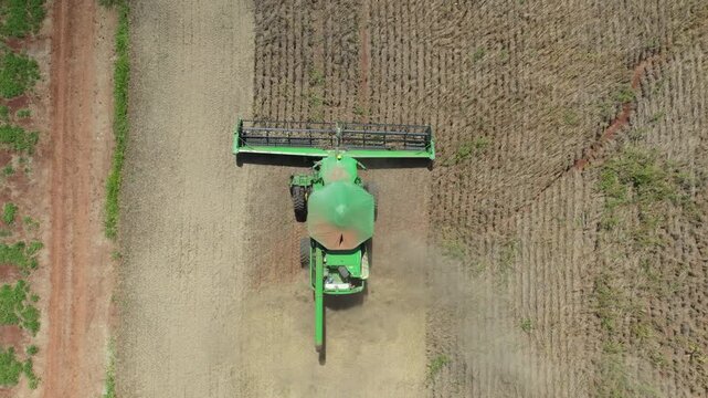 Combine harvester advances through a dry field in a close, symmetric top down aerial tracking shot.
