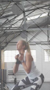 Vertical video: Woman performing kettlebell goblet squats in gym after checking watch for fitness