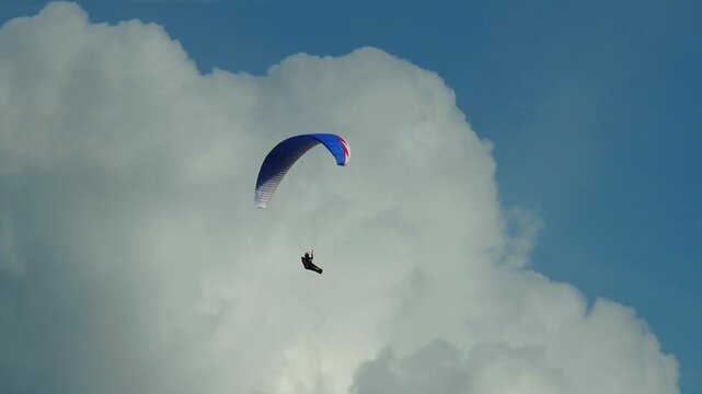 Paraglider gently floats in the sky against a background of beautiful clouds summer day.