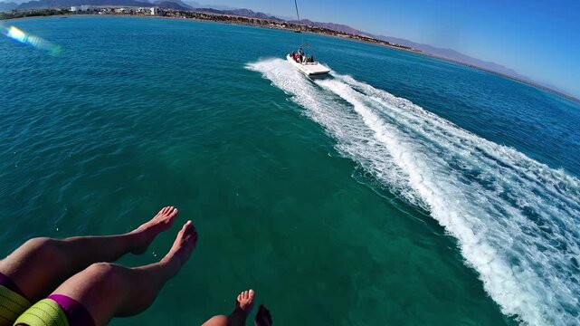 First-person view of parasailing above clear water with coastal hills ahead