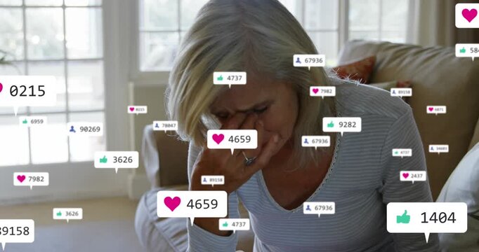 Animation of social media icons over stressed caucasian senior woman crying sitting on the couch
