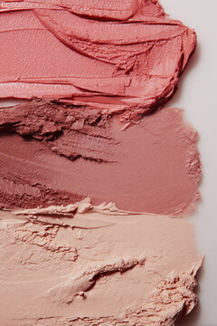 Swatches of pink and nude cosmetic cream textures showing smudged lipstick, foundation, and blush makeup