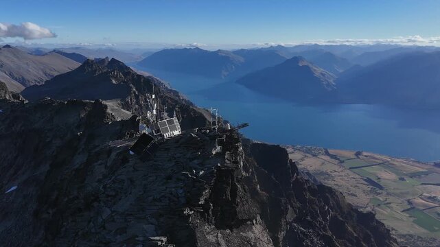 Aerial orbits communication tower on mtn peak above Lake Wakatipu, NZ