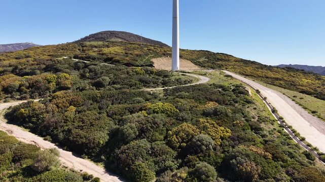 Drone ascent over Mediterranean shrubland toward a lone wind turbine on a mountain ridge
