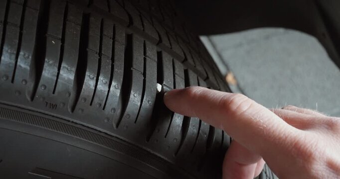 Close-up of a finger pointing at a stone stuck in a car tire tread. Concept of tire damage, safety risk and vehicle inspection.