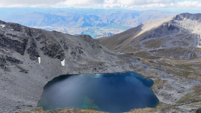 Aerial descends toward dark blue mountain lake on rugged alpine slope