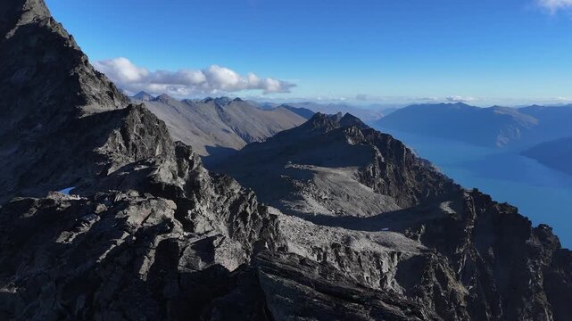 Flyover rugged, jagged mountain alpine summit above lake far below