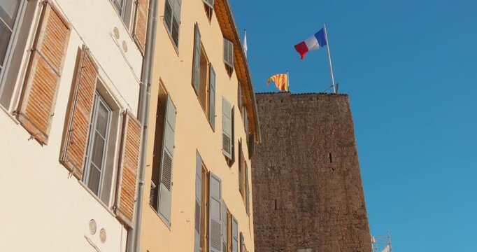 Ancient stone tower with French flag waving against clear blue sky in Grasse, Provence. Historic medieval architecture in world perfume capital of South France with traditional shuttered buildings.