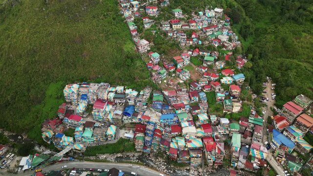 Overhead drone shot of vibrant, clustered, hillside residential houses amid lush greenery - Valley of Colors, Benguet, Philippines