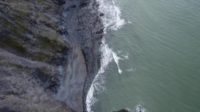 Top down aerial view of Durdle Door coastline with rocky cliffs narrow beach and waves meeting shore showing natural coastal landscape and geology
