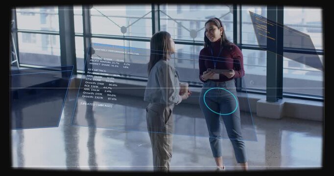 Right woman tapping tablet causing floating business charts around them while peer reviewing data