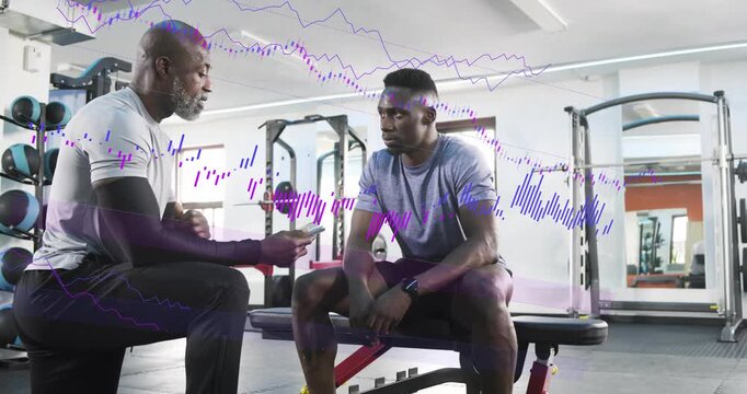 Senior coach kneeling in gym showing device, coaching trainee leaning as purple waveform growing