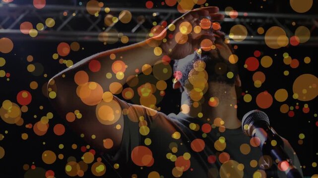 Man on stage at mic picking glass drinking, hydrating, gesturing, animated bokeh floating over him