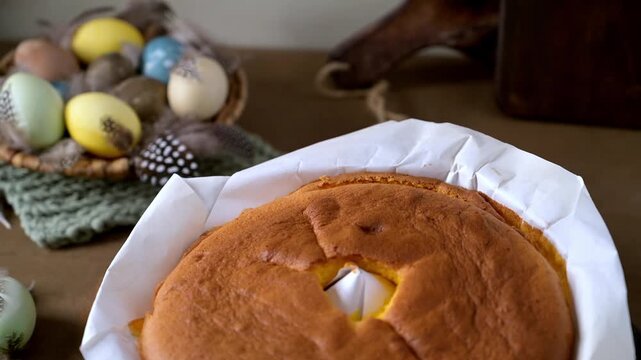 Homemade golden brown Pao de Lo sponge cake rests in parchment paper on a wire rack. Soft natural light highlights the airy texture against a rustic background with decorative Easter eggs.