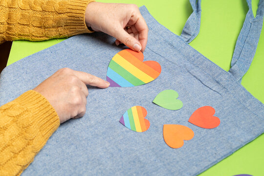 Person decorating a denim tote bag with rainbow and colorful hearts for pride month
